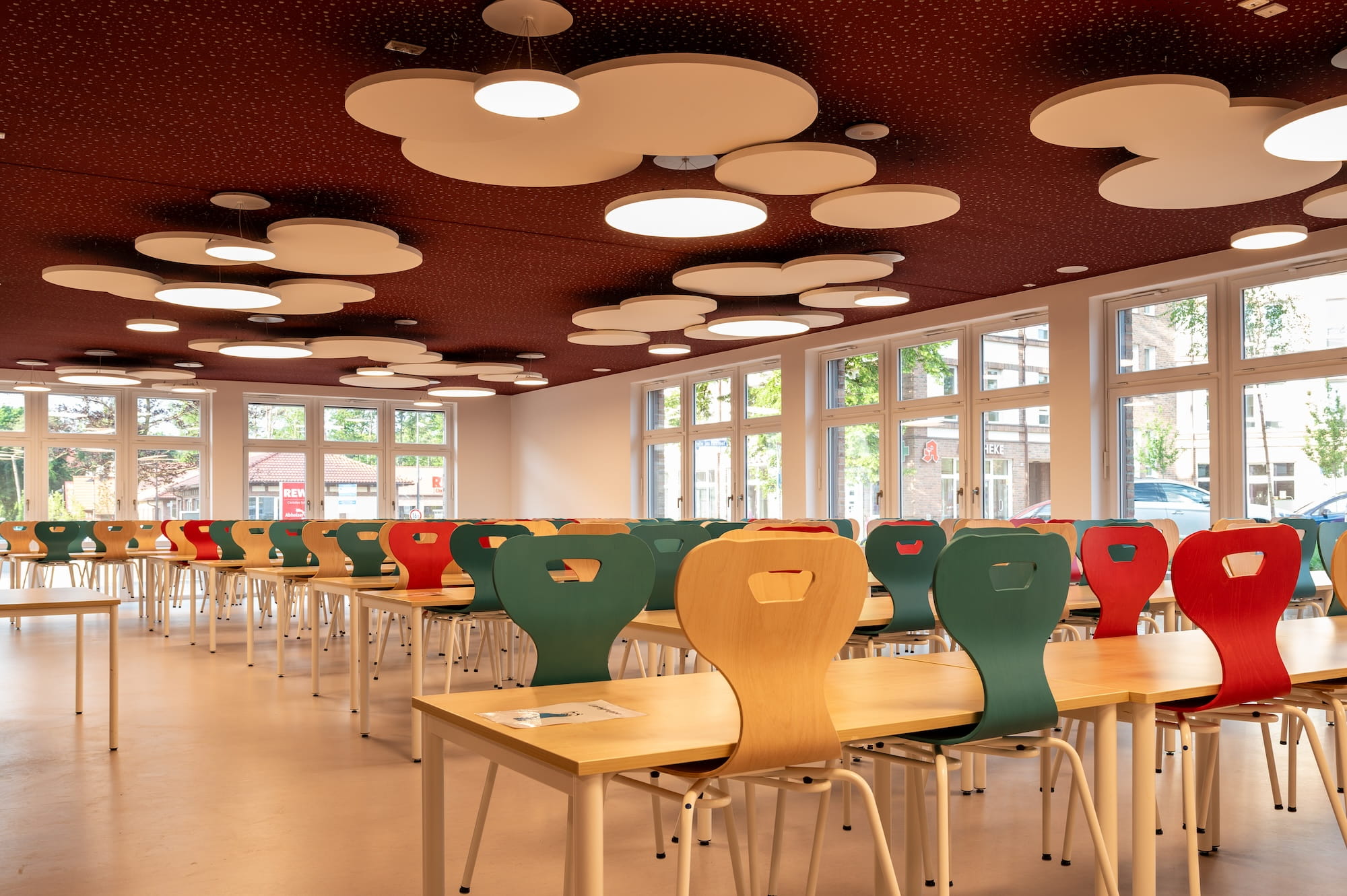 Schulmensa mit Akustikdecke in Wolkenform und bunten Stühlen