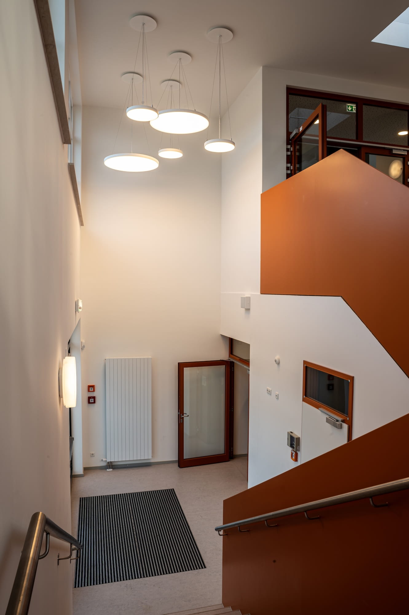 Treppenhaus mit orangefarbener Treppe und runden LED-Pendelleuchten